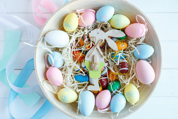 Happy Easter! Bowl with hand painted colorful eggs on white wooden table. Close up. Decoration for Easter, festive background.