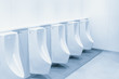 Close up row of urinal toilet blocks in public restroom clean blue color tone.