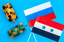 War, Confrontation Concept. Russia, Syria. Tanks Toy Near Russian And Syrian Flag On Blue Background Top View
