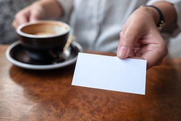 A woman holding and giving a blank empty business card to someone while drinking coffee