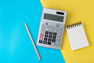 Calculator and notepad on light blue and yellow background