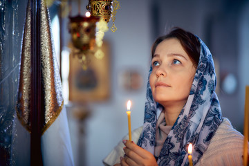 Wall Mural - lifestyle woman lights candles in the Church, praying in front of the icon