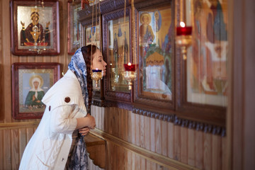 Wall Mural - woman in the Russian Orthodox Church with red hair and a scarf on her head lights a candle and prays in front of the icon.