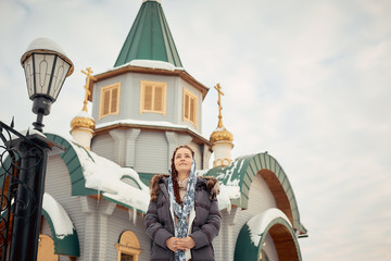 Wall Mural - Russian Orthodox middle-aged woman in a scarf stands on the background of the Orthodox wooden Church.