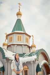 Wall Mural - Russian Orthodox middle-aged woman in a scarf stands on the background of the Orthodox wooden Church.