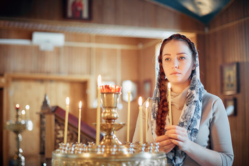 Wall Mural - woman in the Russian Orthodox Church with red hair and a scarf on her head lights a candle and prays in front of the icon.