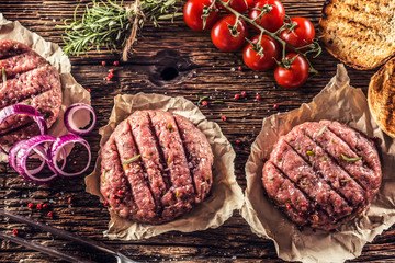 Canvas Print - Raw burgers on wooden table with onion tomatoes herbs and spices