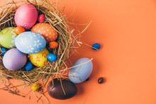 Colorful Easter Eggs With Chocolate And Candies In A Nest On A Orange Background