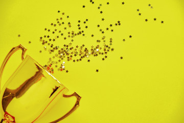 Champion gold cup trophy on yellow background. minimalism style, victory celebration concept. and golden stars of confetti are scattered around