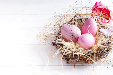 Wall Mural - pink easter eggs in small nest with on white wooden background, copy space