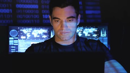 Portrait of developer programmer working on computer in a data center filled with monitor screens.