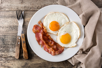 Fried eggs and bacon for breakfast on wooden table. Top view