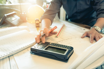 Close up hand of civil engineer people with drawing blueprint  and using calculator for design and planning to budget