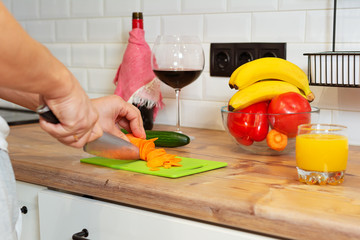 Close-up photo of man hands cooking meal for his wife. Man cuts carrot with knife. Making salad for his wife