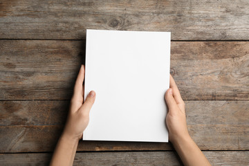 Wall Mural - woman holding brochure with blank cover on wooden background, top view. mock up for design
