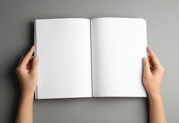 Sticker - Woman holding brochure with blank pages on grey background, top view. Mock up for design
