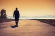 © vvvita - A man walks along a concrete road along the sea at a golden sunset and looks at the mountain