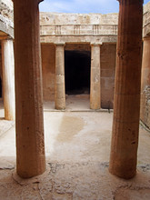 An Underground Chamber At The Tombs Of The Kings In Paphos Cyprus With Old Eroded Sandstone Columns Surrounding A Dark Empty Doorway And Blue Sky