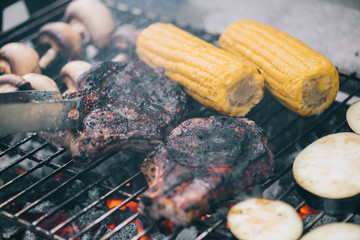 Poster - selective focus of tweezers and juicy tasty steaks grilling on bbq grid with mushrooms, corn and sliced eggplant