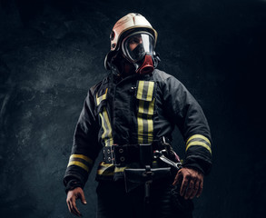 Wall Mural - Portrait of a male in full firefighter equipment. Studio photo against a dark textured wall