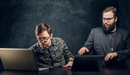 Two professional programmers work in the office against the background of the dark wall