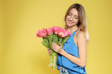 Fototapeta Tulipany - Portrait of beautiful smiling girl with spring tulips on yellow background, space for text. International Women's Day