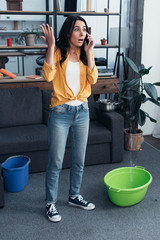 Wall Mural - Full length view of shocked woman talking on phone while water leaking from ceiling