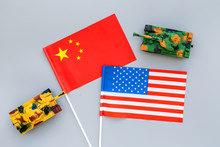 War, Confrontation Concept. China, USA. Tanks Toy Near Chinese And American Flag On Grey Background Top View