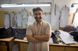 © IndiaPix - Happy looking tailor standing in his workshop with arms crossed.