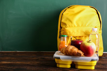Schoolbag And Lunch Box With Tasty Food On Table