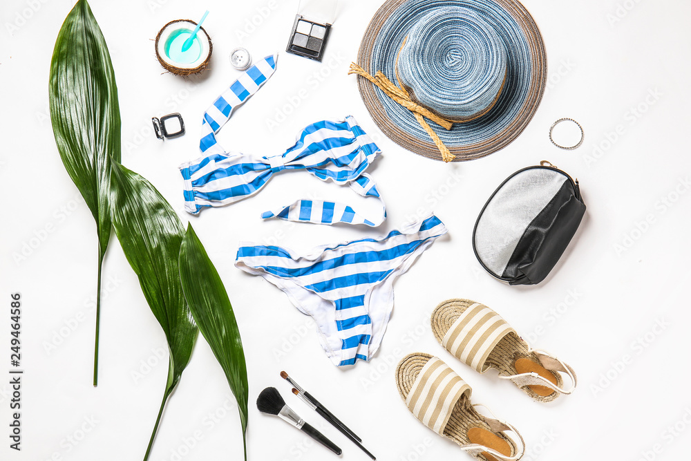 Female clothes with makeup cosmetics and tropical leaves on white background