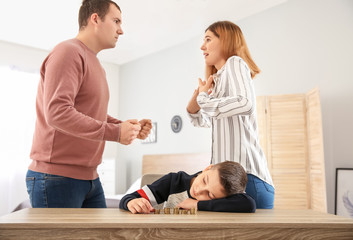 Wall Mural - Sad little boy with coins and his quarreling parents at home. Concept of child support