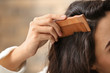 Woman combing hair on blurred background, closeup
