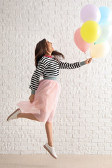 Canvas Print - Jumping young woman with balloons against white brick wall