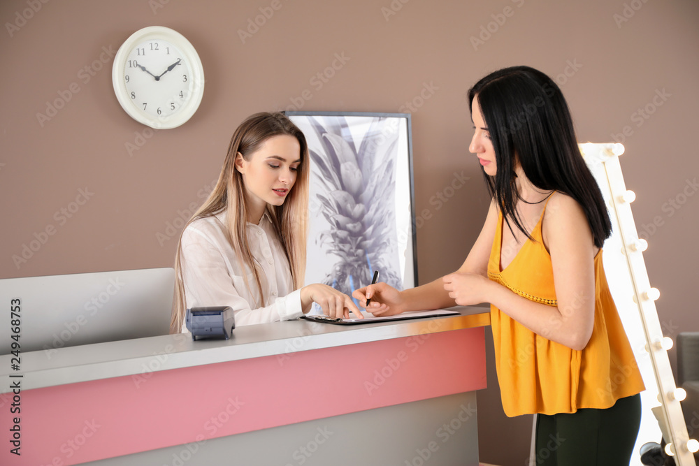 Young woman booking room in hotel at reception