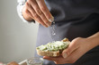 © Pixel-Shot - Young woman sprinkling cheese onto piece of fresh bread with green butter, closeup