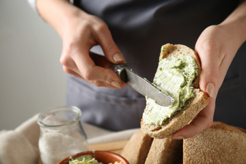 Young woman spreading green butter on piece of fresh bread at table, closeup