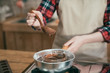 © PR Image Factory - Fondue with melting chocolate in pot on stove. focus female hands holding wooden spoon cooking stirring cocoa sweet in kitchen. valentine day dessert preparing as gift present indoor at home.