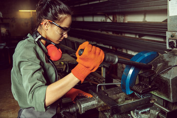 Wall Mural - Busy and serious craftswoman grinding timbers with special machine. Beautiful woman wearing safety glasses. Concept of joiner's shop and woodworking. Gender equality. Male profession