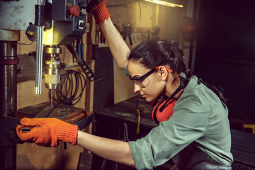 Wall Mural - Busy and serious craftswoman grinding timbers with special machine. Beautiful woman wearing safety glasses. Concept of joiner's shop and woodworking. Gender equality. Male profession