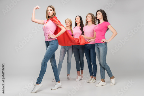 Fotografía confident girl wearing red superhero cape showing muscle near attractive women o