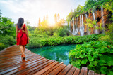 Woman traveler walking on wooden path trail with lakes and waterfall landscape in Plitvice Lakes National Park, UNESCO natural world heritage and famous travel destination of Croatia.