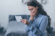 © LIGHTFIELD STUDIOS - grieving woman holding photograph, covering mouth with hand and crying at home through window with raindrops