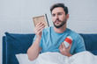 sad man lying in bed and holding photo frame with funeral urn
