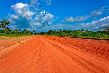 Typical red soils unpaved rough countryside road in Guinea, West Africa.