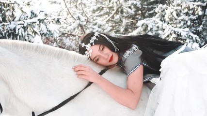 Wall Mural - dark-haired girl gently and tenderly falls on a white horse, softly strokes animal hair and smiles mysteriously, a fallen angel in love takes the bright side, a lady with black hair and a gray cloak