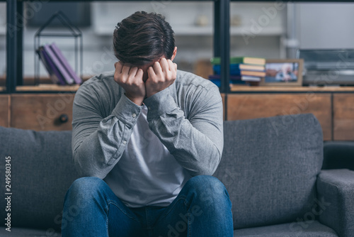 Photographie man sitting on couch, crying and and covering face with hands at home
