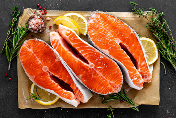 Wall Mural - Fresh raw salmon fish steaks on black background with ingredients for cooking. Closeup. Top view