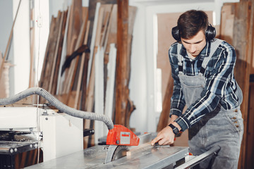 Canvas Print - A man carves a tree. The carpenter works with saw in a studio. An engineer provides a tree shape