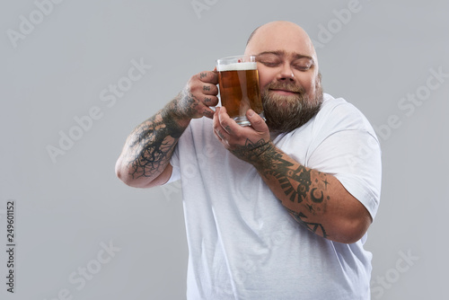 Waist up of bearded tattooed man pressing glass of beer to his cheek © Yakobchuk Olena